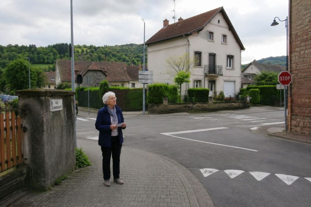 Elderly person standing at a quiet street corner, looking around as if trying to recognize the way home.